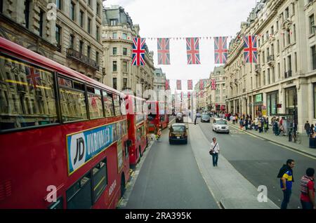 Britische Flaggen schmücken eine belebte Londoner Straße, an der berühmte schwarze Taxis und rote Doppeldeckerbusse vorbeifahren. Britische Flaggen schmücken die Straßen für Krönungen und Jubiläen Stockfoto