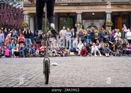 Covent Garden Market mit Menschenmassen, auf denen ein Künstler, Straßenkünstler, auf einem Einrad oder einem Einrad zu sehen ist. Familien genießen die Show an diesem geschäftigen Platz Stockfoto