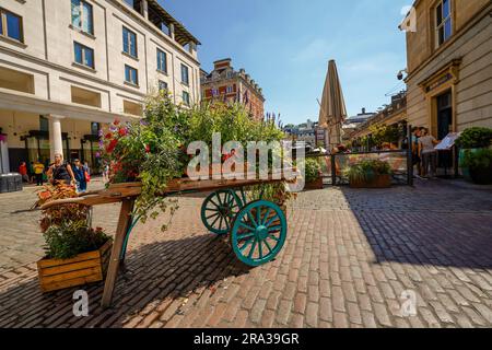 Covent Garden Market Schild in einem antiken Holzwagen, umgeben von Blumen. Der Londoner Covent Garden Market Square ist bei Touristen und Einheimischen beliebt. Stockfoto