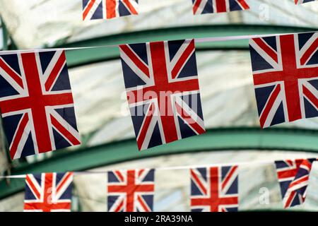 Britische Flaggen hängen im Covent Garden, einem beliebten Freiluftmarkt in London mit Geschäften, Restaurants und Bars. Nahaufnahme von Union-Jack-Flaggen, die herumtrampeln, fliegen. Stockfoto