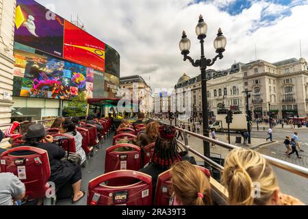 Touristen fahren in einem berühmten roten Doppeldeckerbus durch den Piccadilly Circus, einen berühmten belebten Platz in London. Beste Aussicht auf die Stadt vom offenen Bus. Stockfoto