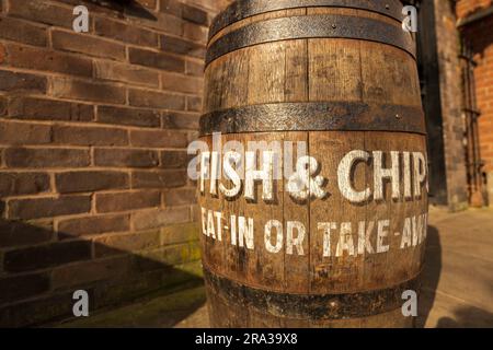 Ein traditionelles englisches Pub-Schild mit der Werbung für Fish and Chips zum Essen im Restaurant, zum Mitnehmen. Das Schild ist auf einem Holzfass gemalt und hat ein nostalgisches Aussehen Stockfoto