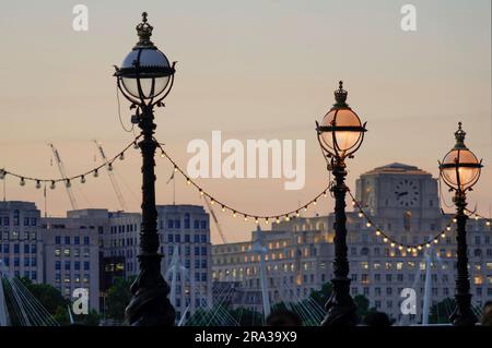 Spaziergang auf der Themse in London in der Abenddämmerung mit dekorativen Lampenpfählen. Einige der Straßenlichter sind an, während andere ausgeschaltet sind. Eine kaputte Ampel. Stockfoto