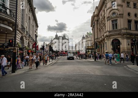 Belebte Londoner Straße am Piccadilly Circus mit dem berühmten schwarzen Taxi im Zentrum, roten Doppeldeckerbussen und vielen Pendlern, Touristen im Hintergrund. Stockfoto