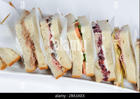 Club-Sandwich, das von Zahnstochern zusammengehalten wird und aus vielen leckeren Zutaten und Saucen besteht, auf weißem Teller und Hintergrund Stockfoto