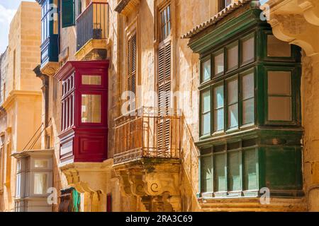 Valletta, Malta: Traditionelle farbenfrohe maltesische Fenster und Balkone in Rot, Grün und Blau sowie gelbe Wände an einem sonnigen Tag in der Hauptstadt von Malta Stockfoto