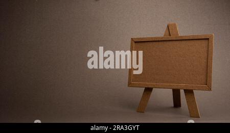 Eine leere braune Holztafel auf einer Staffelei auf grauem Hintergrund Stockfoto