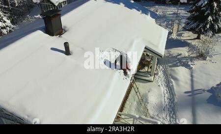 Drohne über einem Hausbesitzer, der Schnee putzt und schaufelt, Solarpaneele auf einem Hausdach Stockfoto