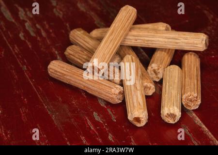 Ein Stapel von Passstiften auf rotem Hintergrund, Passstifte zum Verbinden von zwei Holzstücken, Gelenken, Schreinern Stockfoto