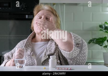 Ältere Frau nimmt Pillen in der Küche zu Hause. Alleinstehende Frau im Ruhestand, drinnen Stockfoto