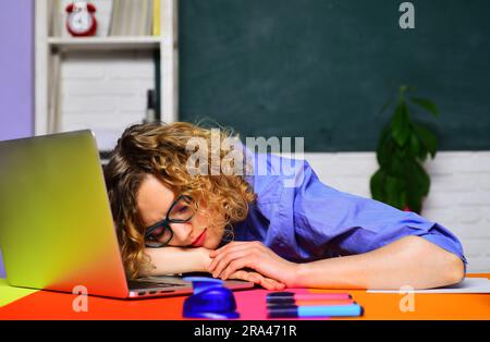 Müde, überarbeitete Lehrerin, die auf dem Schreibtisch im Klassenzimmer schläft. Zurück in die Schule. Wissenstag. Student bereitet sich auf die Universitätsprüfung vor. Lernen und Stockfoto