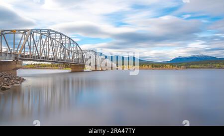 Große, von Menschenhand geschaffene Stahlbrücke, die sich über die Nisutlin Bay in der Ortschaft Teslin erstreckt und im Frühling zum Yukon River im Norden Kanadas floss Stockfoto