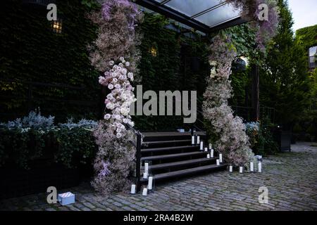 Wunderschöne Blumenarrangements mit Blumenstrauß-Hochzeit mit Rosen, Kerzen und dem Atem des Babys in einem üppigen botanischen Garten mit Treppe und Bogen. Stockfoto