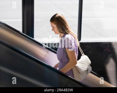 Belgrad, Serbien - 15. Juni 2022: Junge elegante Frau in lila Kleidung, die an einem sonnigen Tag auf die U-Bahn-Rolltreppe steigt Stockfoto