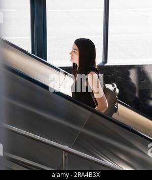 Belgrad, Serbien - 15. Juni 2022: Junge Frau in Schwarz, die an einem sonnigen Tag auf die U-Bahn-Rolltreppe steigt Stockfoto