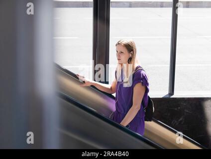 Belgrad, Serbien - 15. Juni 2022: Junge Frau in lila Kleidung, die an einem sonnigen Tag auf die U-Bahn-Rolltreppe steigt Stockfoto