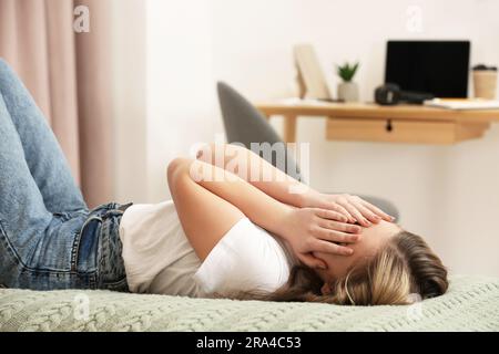 Unglückliches Teenager-Mädchen, das zu Hause das Gesicht mit den Händen am Bett bedeckt Stockfoto