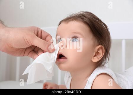 Vater wischte die laufende Nase eines kleinen Babys mit Serviette auf dem Bett, Nahaufnahme Stockfoto