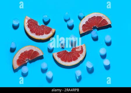Grapefruitscheiben mit Eiswürfeln auf blauem Hintergrund Stockfoto