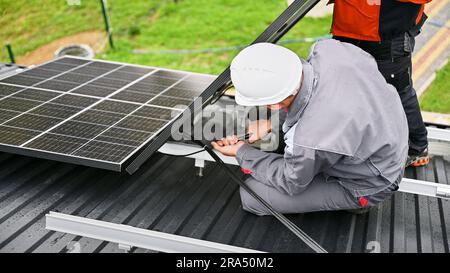 Stellt bei der Installation von Solarpaneelen auf dem Dach des Hauses Kabel an. Arbeiter, die PV-Solarmodule auf dem Dach montieren. Konzept alternativer und erneuerbarer Energien. Stockfoto