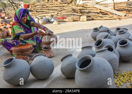 TIKAMGARH, MADHYA PRADESH, INDIEN - 13. AUGUST 2022: Portrait einer glücklichen traditionellen indischen Töpferin, die auf Tontopf malt. Stockfoto