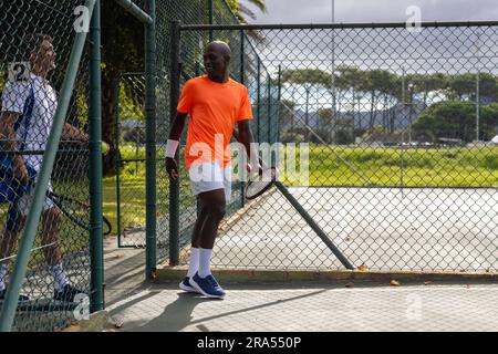 Fröhliche, vielseitige Tennisspieler mit Sporttasche und Schlägern, die sich auf dem Freiluftplatz unterhalten, Kopierbereich Stockfoto