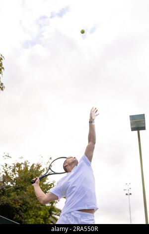 Weißer männlicher Tennisspieler, der an bewölkten Tagen Tennis spielt und auf dem Platz im Freien Ball spielt, Kopierbereich Stockfoto