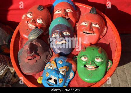 Holzmaske mit lustigen Gesichtern und wütendem Gesicht in einem Korb auf dem Markt von Nepal zum Verkauf gehalten. Farbenfrohe Holzmasken-Sammlung Stockfoto