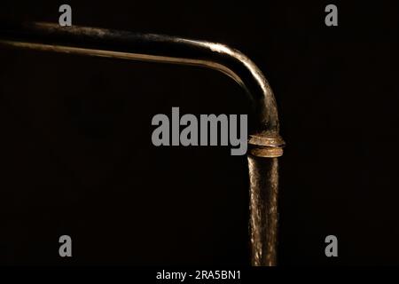 Wasser fließt aus einem alten, dreckigen Wasserhahn im Dunkeln, auf schwarzem Hintergrund Stockfoto