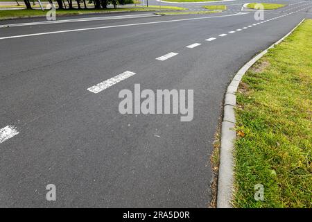 Straßenmarkierungssystem. Leine auf dem Asphalt. Betonaufkantung und Rasen. Kreisverkehr im Hintergrund. Stockfoto