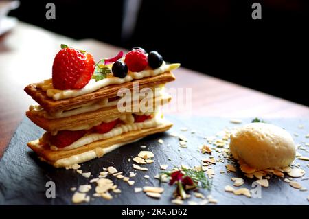 Erdbeere Heidelbeere Himbeermille Feuille mit Eiskugel auf schwarzem Schieferteller delikates Café Dessert Stockfoto