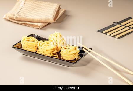 Chinesische Nudeln auf schwarzem Teller und Bambusstäbchen. Stockfoto