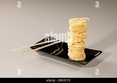 Ein Stapel chinesische Nudeln auf schwarzem Teller und Bambusstäbchen. Stockfoto