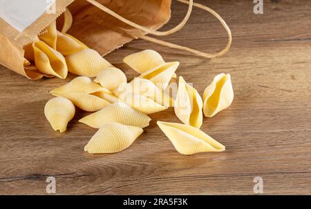 Italienische Küche. Teigwaren in Form einer Schale werden aus der Verpackung auf dem Tisch gegossen. Stockfoto