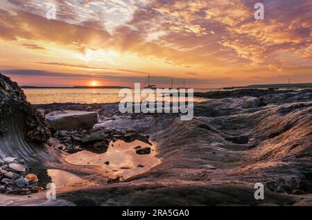 Die Sonne geht über dem Vorgewende unter und beleuchtet die verwitterten Stein- und Felsenbecken, die sich auf dem Küstenweg befinden, der von Appledore nach No verläuft Stockfoto