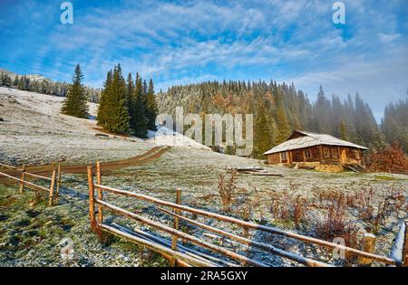 Herbst Landschaft mit den ersten unerwarteten Schnee und Herbst Laub. Alte Holzhütten auf einem berghügel Stockfoto