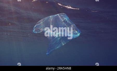 Blauer Einweg-Plastikbeutel schwimmt unter der Oberfläche in blauem Wasser bei Sonneneinstrahlung. Plastiktüte, die ins Meer geworfen wurde, treibt am Morgen unter der Oberfläche von blauem Wasser Stockfoto