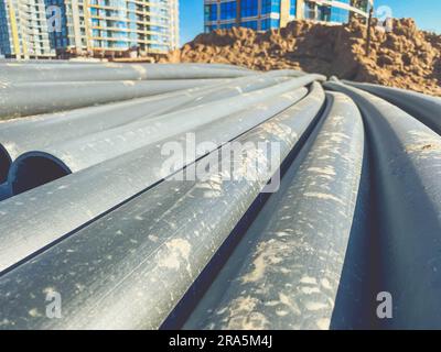 Rohre für den Aufbau der Kommunikation im neuen Mikrobezirk. Schwarze Kunststoffrohre in Sand und Schmutz. Lange Rohre für die Wasser- und Abfallentsorgung Stockfoto