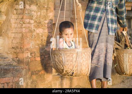 Eine birmanische Frau, die ein Kind und Holz im Korb über der Schulter trägt, Bagan, Birma, Pagan, Myanmar Stockfoto