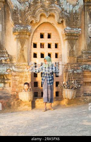 Eine birmanische Frau, die ein Kind und Holz im Korb über der Schulter trägt, Bagan, Birma, Pagan, Myanmar Stockfoto