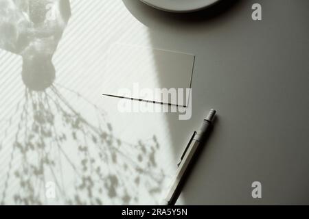 Weißes, leeres Visitenkartenmodell, Vorlage an der Ecke des Tisches mit Tageslicht und Schatten. Schatten der Blumen in der Vase auf dem Tisch. Stockfoto