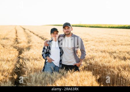 Ein paar Bauern in karierten Hemden und Kappen stehen bei Sonnenuntergang auf dem Weizenfeld. Stockfoto