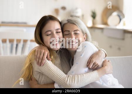 Positiv liebevolles Teenager-Mädchen, das Oma mit geschlossenen Augen umarmt Stockfoto