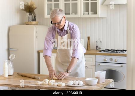 Ein älterer Bäckermann, der Haushaltsschürze trägt und rohen Teig pflastert Stockfoto