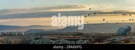 Ein Panoramabild von Heißluftballons, die über den Goreme Historical National Park fliegen, und von denen einige aus dem Love Valley aus aufgeblasen werden Stockfoto