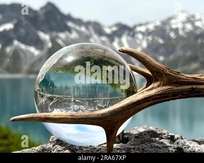 Röhrengeweih neben Linsenkugel, Kristallkugel, mit Reflexionen des Luenersee (Lünersee, Montafon, Vorarlberg). Stockfoto