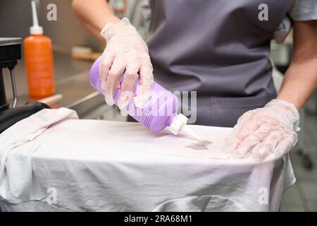 Frau in Schutzhandschuhen, die Lösungsmittel in den Fleck auf dem T-Shirt aufträgt Stockfoto