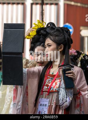 Hongkong, China -- 11. März 2023. Zwei junge Frauen, die traditionelle chinesische Hochzeitskleidung tragen, untersuchen sich im Spiegel. Stockfoto