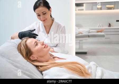 Junger Arzt in Uniform führt eine Injektion um die Augen durch Stockfoto