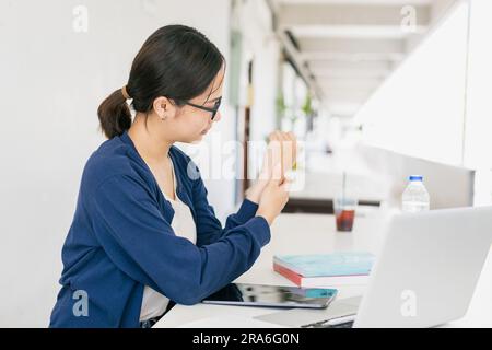 Junge Assianerin Muskel-Sehnen-Gelenkschmerzen durch Laptop-Computer-Massage zur Schmerzlinderung. Stockfoto